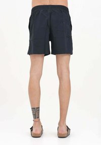 Pantaloni da bagno blu navy con vita elasticizzata, tasche laterali e tasca posteriore con patta. Tessuto leggero con una superficie liscia.