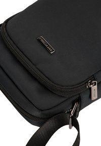 Pochette in tessuto nero con texture liscia, chiusura a zip e un'etichetta metallica con marchio; presenta una tracolla rimovibile e cuciture robuste.