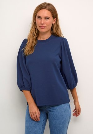 Marineblaue Struktur-Oberteil mit kurzen, gepufften Ärmeln und rundem Ausschnitt, kombiniert mit hellblauen Jeans. Einfaches, lässiges Design.