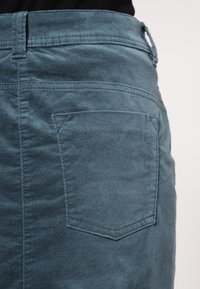 Falda azul oscuro hecha de un tejido suave y texturizado. Presenta un único bolsillo trasero con un contorno cosido y una cintura para el ajuste.
