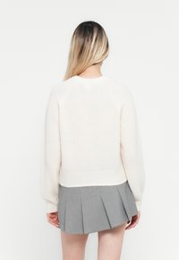 Lichtbeige trui van zachte stof, met een cropped ontwerp, raglanmouwen en een geribbelde zoom, gecombineerd met een grijze geplooide rok.