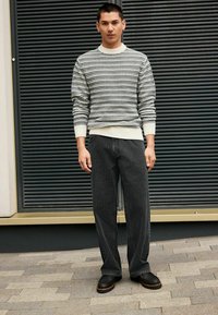 Maglione lavorato a maglia in crema con motivo nero, abbinato a jeans a gamba larga grigio scuro e stivaletti neri con suola testurizzata.