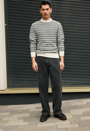 Knit sweater in cream with black pattern, paired with dark gray wide-leg jeans and black ankle boots with a textured sole.