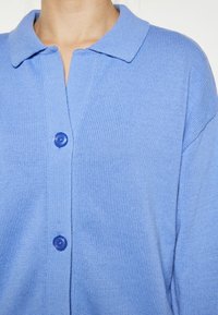 Cardigan a maglia azzurro chiaro con colletto, dotato di chiusura a bottoni e texture a coste. Tessuto morbido e design con vestibilità rilassata.