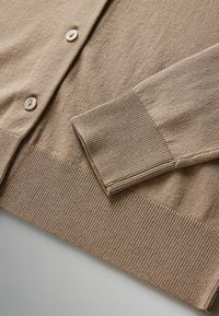 Lichtbruine cardigan van zachte stof, met een geribbelde zoom en manchetten, en vijf ronde knopen langs de voorkant.