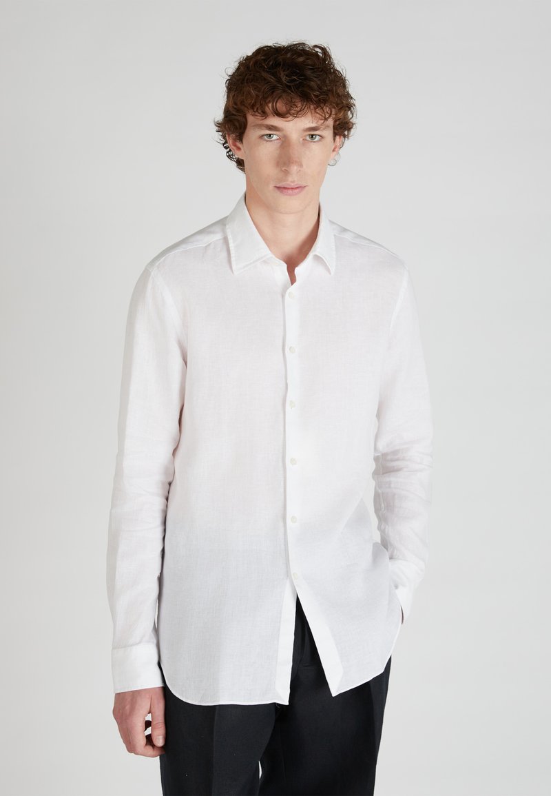 White linen button-up shirt with long sleeves and a pointed collar. Features a slightly curved hem and a relaxed fit.