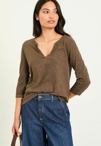 Brown, long-sleeve V-neck shirt with buttons, paired with high-waisted blue jeans. The shirt features a soft, textured fabric.