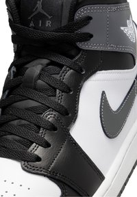 Zapatilla alta en blanco y negro, hecha de cuero y textil, con detalles en gris, cordones redondos y un logo bordado.