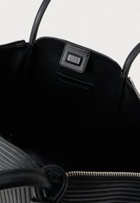 Närbild av en öppen svart läderhandväska som visar insidan, sydd märke, dragkedja och två rundade handtag.