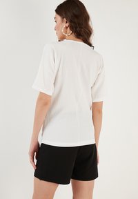 Witte textuur korte mouwen top met een relaxte fit, gecombineerd met zwarte shorts. Opvallende details zijn een gebogen zoom en subtiele stiksels.