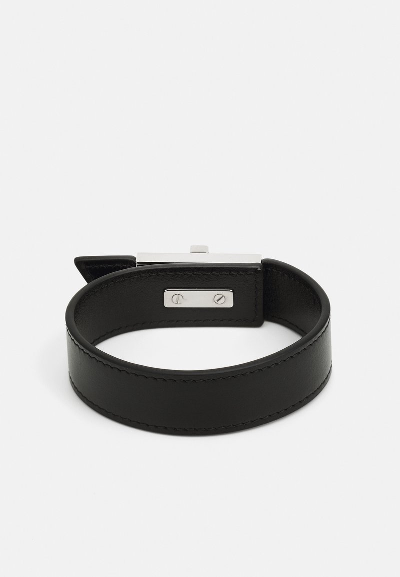 Schwarzes Lederarmband mit glatter Textur, runder Form und einem silbernen Metallverschluss mit dekorativen Akzenten auf beiden Seiten.