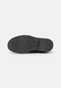 Suela de zapato de goma negra con patrones texturizados para agarre. Presenta ranuras y un logotipo redondo en el talón. Diseño duradero y antideslizante.