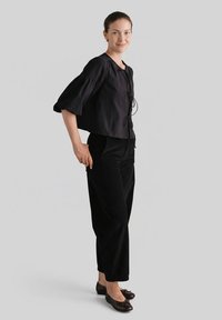 Czarny krótki top z rozkloszowanymi rękawami, związany z przodu. Do tego czarne spodnie sztruksowe. Stylizację dopełniają brązowe baleriny z kokardką.