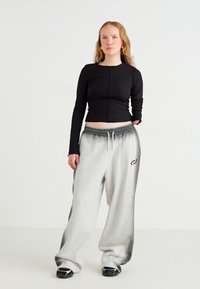 Schwarzes, kurzes Langarmtop, kombiniert mit grauen, übergroßen Sweatpants mit einem dunklen Farbverlauf und einem Logo-Detail am linken Oberschenkel.