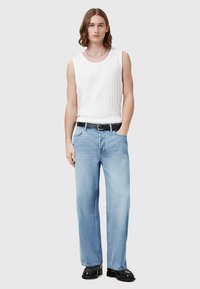 Bela rebrasta majica brez rokavov, svetlo modre kavbojke s ravnimi hlačnicami, črni pas in črni čevlji. Oprijet kroj z osnovnimi kovinskimi detajli in gladko teksturo.