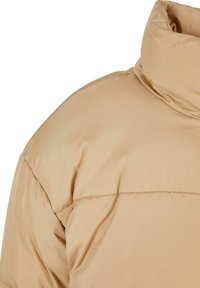 Beige pufferjakke med høy krage, laget av glatt, blankt stoff med subtile sømmer langs skuldrene og sømmene.