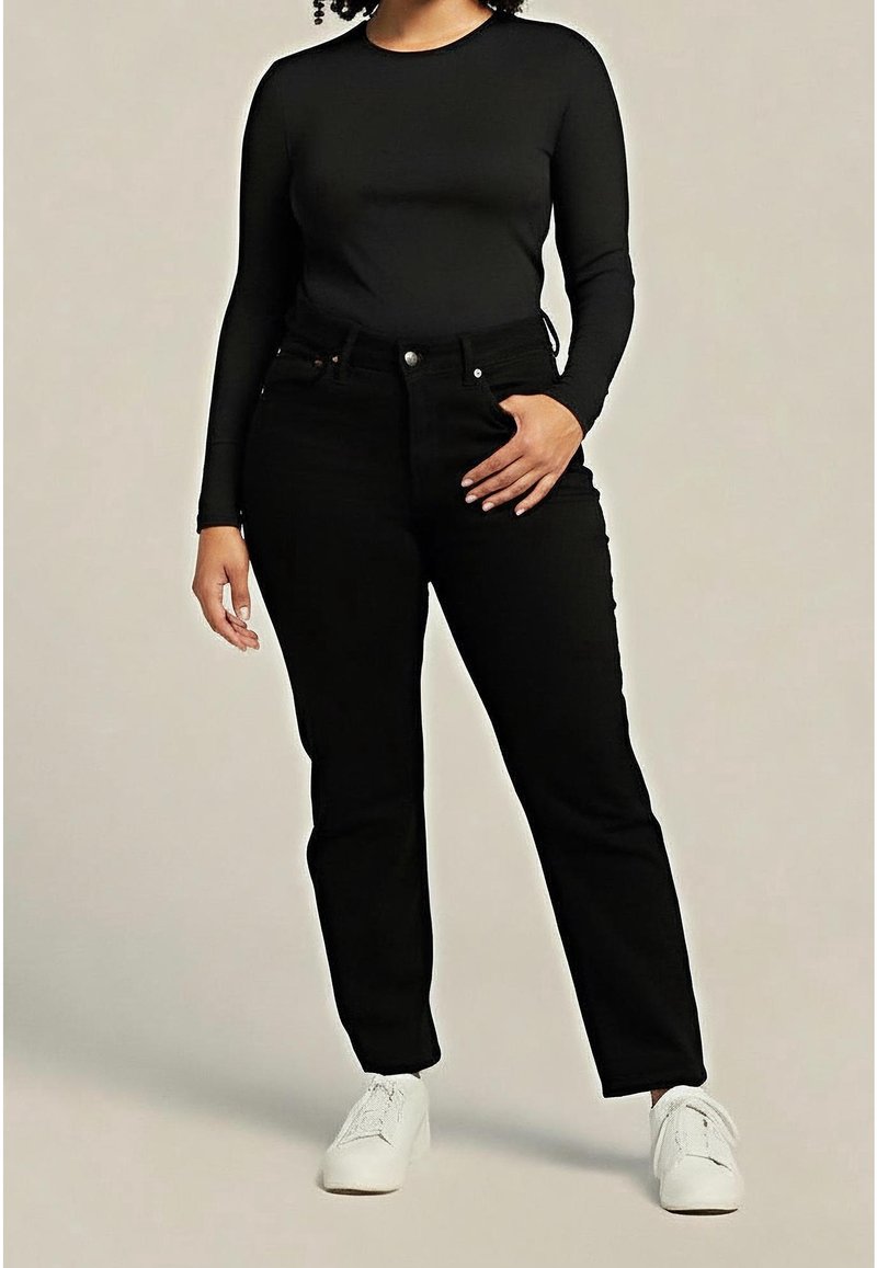 Top negro de manga larga combinado con jeans negros de tiro alto y zapatillas blancas. Los jeans tienen un diseño clásico de cinco bolsillos y un ligero elastano.