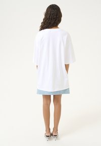 Witte oversized t-shirt met korte mouwen, gemaakt van zachte katoen, en een gebogen zoom. Gecombineerd met een lichtblauwe denimrok en zwarte instapschoenen.