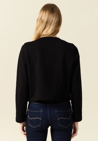 Zwart cropped sweatshirt met een ronde halslijn en lange mouwen, gecombineerd met donkerblauwe jeans met twee achterzakken en stikdetails.