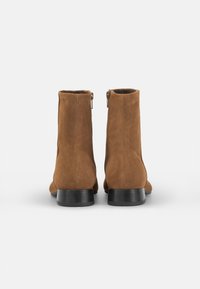 Botines de ante marrón con una textura suave, cierre de cremallera y tacones cuadrados negros, que presentan un diseño simple y elegante.