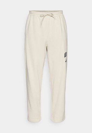 Beige sweatpants med elastisk talje og snor, tætsiddende ben og sort Adidas-logo på øverste venstre lår.