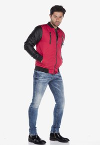 Rode bomberjack met zwarte leren mouwen, geribbelde manchet en kraag. Slim-fit vervagende blauwe spijkerbroek gecombineerd met glanzende zwarte enkellaarsjes.