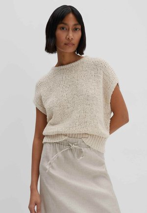 Knit cream top with textured surface, loose fit, and short sleeves. Paired with a light-colored, drawstring waist skirt.