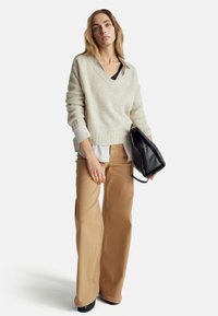 Béžový svetr s výstřihem do V, vrstvený přes bílo-modrou pruhovanou košili. K šatům se hodí béžové kalhoty širokého střihu a černá kabelka.