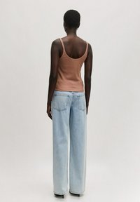 Brauner ärmelloser Oberteil mit taillierter Passform, kombiniert mit hellblauen High-Waist-Jeans mit weitem Bein, die zwei Gesäßtaschen und eine glatte Textur aufweisen.