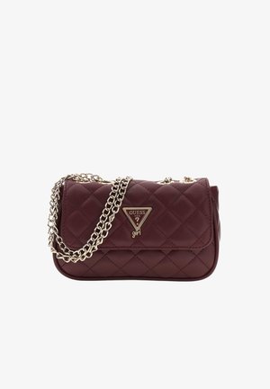 Sac à main matelassé Guess marron foncé avec plaque logo triangulaire dorée et bandoulière chaîne dorée sur fond blanc.