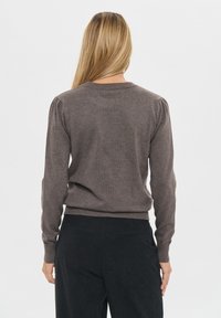 Ruskea neulepusero pitkillä hihoilla, ribbausatkailla ja hienovaraisilla puffiyksityiskohdilla olkapäissä, nähtynä takaa valkoista taustaa vasten.