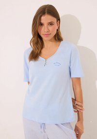 Chemise en coton bleu clair à col en V avec des manches courtes, ornée de trois boutons décoratifs et d'un texte brodé "Club" sur la poitrine.
