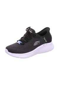 Chaussure de sport en mesh noir avec un bout arrondi, semelle blanche et détails texturés. Équipée de lacets noirs et d'un logo de marque sur le côté.