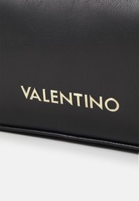 Svart läderhandväska med en upphöjd gold "VALENTINO"-logotyp. Slät yta med en strukturerad form och rena kanter.