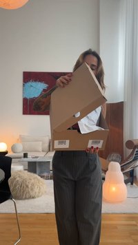 Boîte en carton brun uni avec un rabat supérieur partiellement ouvert, révélant du papier de soie blanc froissé à l'intérieur. Code-barres visible sur le côté de la boîte.