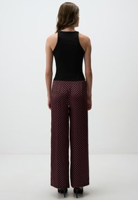 Zwarte geribbelde tanktop gecombineerd met wijde, patroonbroek in rood en marineblauw, met een geometrisch ontwerp en subtiele textuur.