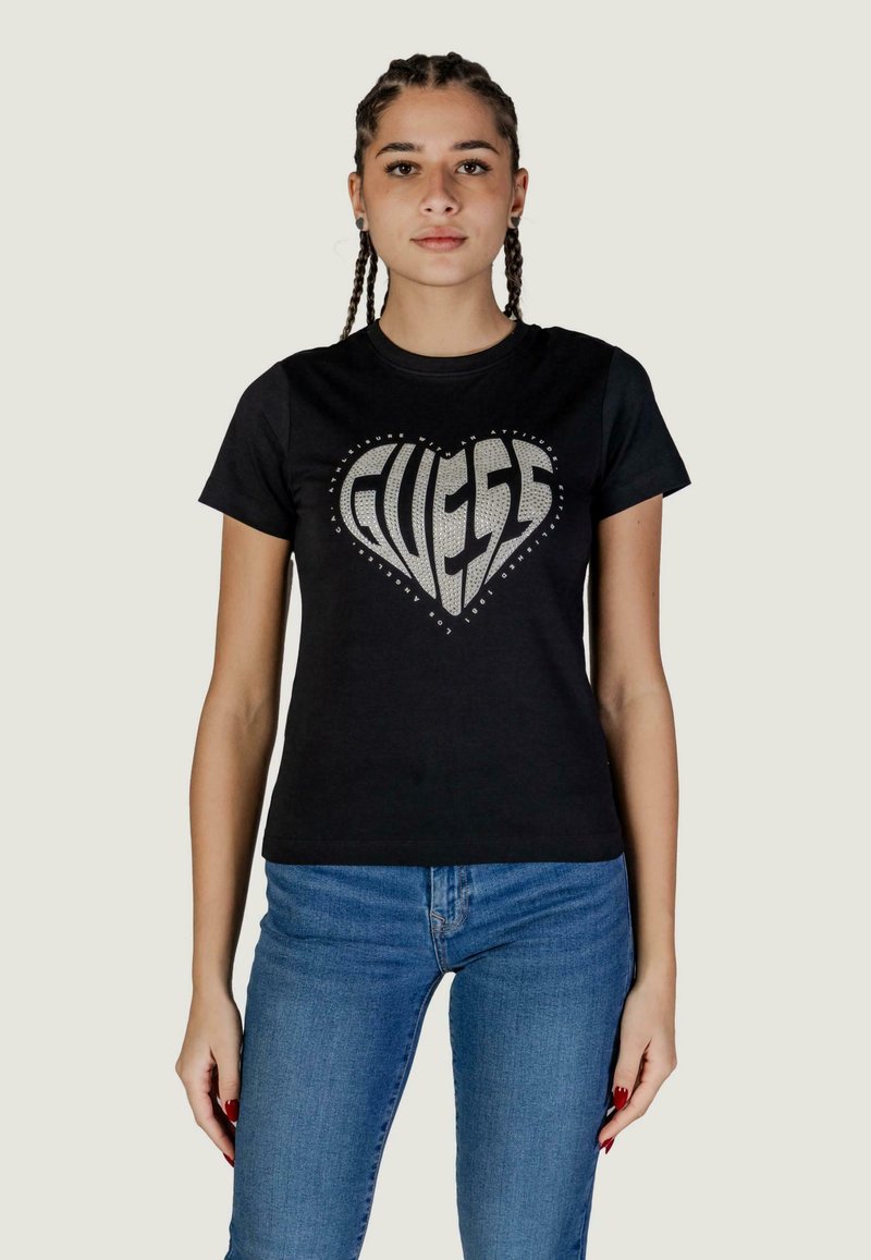 T-shirt nera in cotone con logo "GUESS" a forma di cuore in metallo argentato, arricchito da strass, collo rotondo e maniche corte.