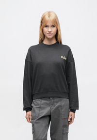 Μαύρη cropped φούτερ με  μακριά μανίκια και στρογγυλή λαιμόκοψη, με χρυσό κεντημένο λογότυπο στο αριστερό στήθος. Απαλή υφή.