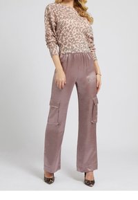 Sweter w szpic w kolorze jasnoróżowym i brązowym, zestawiony z satynowymi spodniami typu wide-leg w kolorze mauve, które mają boczne kieszenie. Szpilki w panterkę z wydłużonym noskiem.