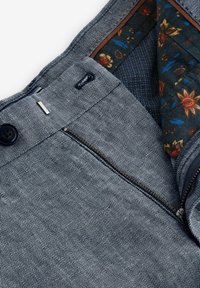 Pantalons rayés bleu foncé avec fermeture éclair et bouton. Doublés d'un tissu à motif florale, mettant en avant des motifs et textures complexes.