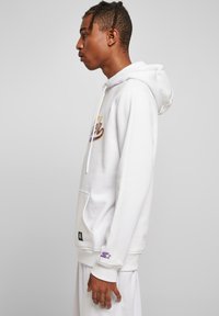 Hoodie en coton blanc avec une poche avant, texte graphique violet et détail de logo sur la manche. Comprend une capuche avec cordon de serrage et des poignets côtelés.