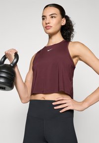 Maroon sleeveless athletic crop top with a circular neckline, featuring a small white Nike logo, paired with black high-waisted leggings.