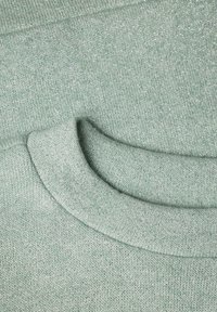 Gros plan d'un tissu tricoté vert clair avec un col rond montrant la texture et les détails des coutures.