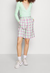 Jasnozielona bluzka z długimi rękawami, zestawiona z kratkowymi szortami w pastelowe różowe i zielone kolory. Wyraźne plisy i boczne kieszenie. Białe trampki.