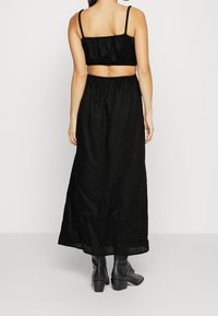 Černý lněný dvoudílný set s krátkým topem na tenkých ramínkách a splývavou maxi sukni. Nosen s kotníkovými botami, které ukazují jednoduchý design.