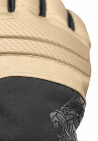 Lähikuva vaaleasta pehmustetusta hanskasta mustalla kankaalla, jossa on geometrijen leijonamerkki ranteen alueella.