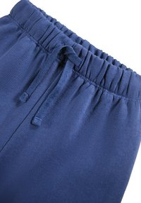 Navy blauwe sweatpants hebben een geribde tailleband met een verstelbaar trekkoord. De stof is glad met een zachte textuur en zonder zichtbare patronen.
