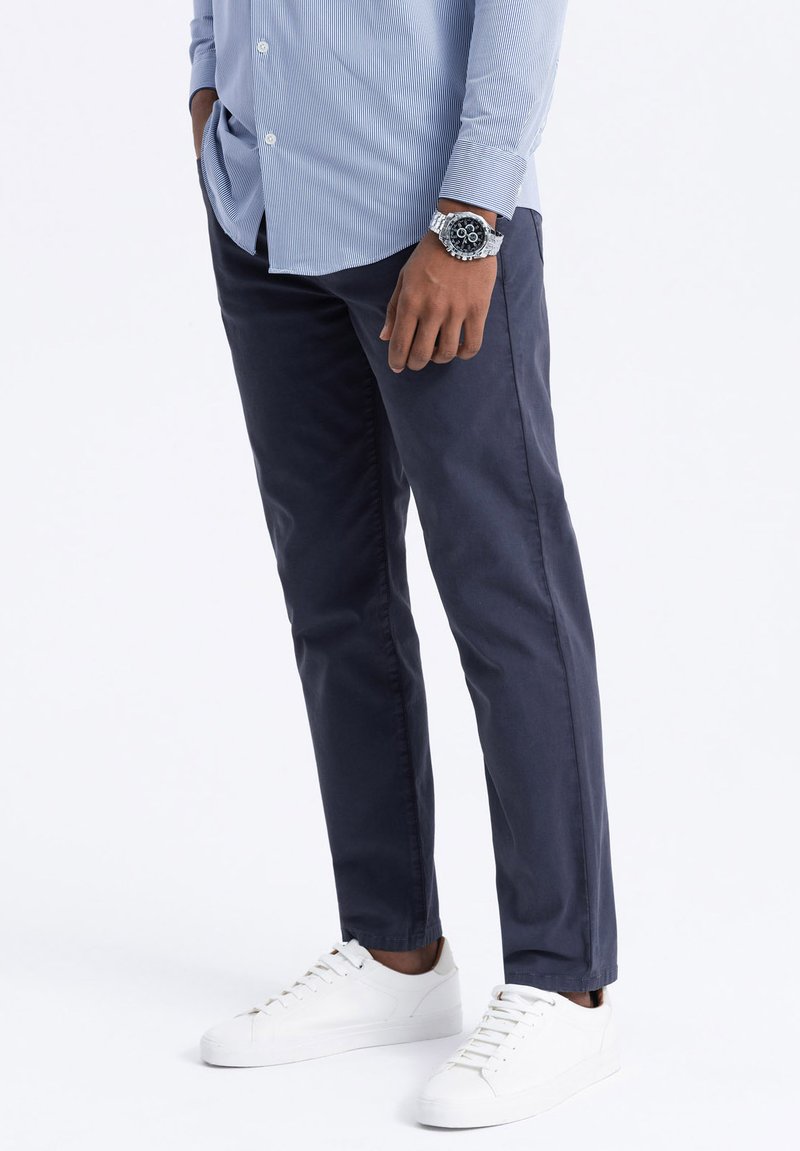 Pantalon bleu marine en coton avec une texture lisse. Présente une coupe slim, des poches latérales et est associé à des baskets blanches.