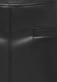 Détail d’un vêtement en cuir noir avec une couture verticale et une poche fendue horizontale sur une surface lisse du matériau.