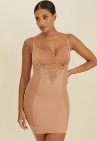 Nude shapewear klänning med spetsdetaljer vid bysten och nederkanten, med justerbara axelband och figursydd silhuett. Slät tygtextur.